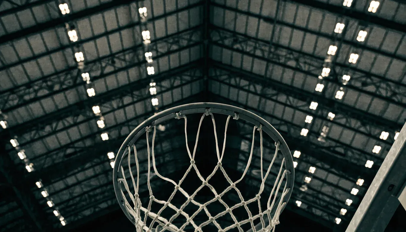 Ein Basketballkorb von unten gesehen, darüber eine Hallendecke mit Scheinwerfern und Stahlträgern.