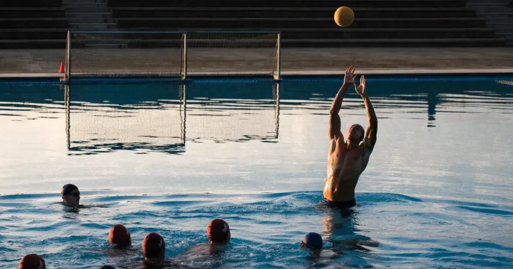 Ein Wasserballbecken am Abend mit zwei schwimmenden Torrahmen an den Enden, ruhiges blaues Wasser, leere Ränge.